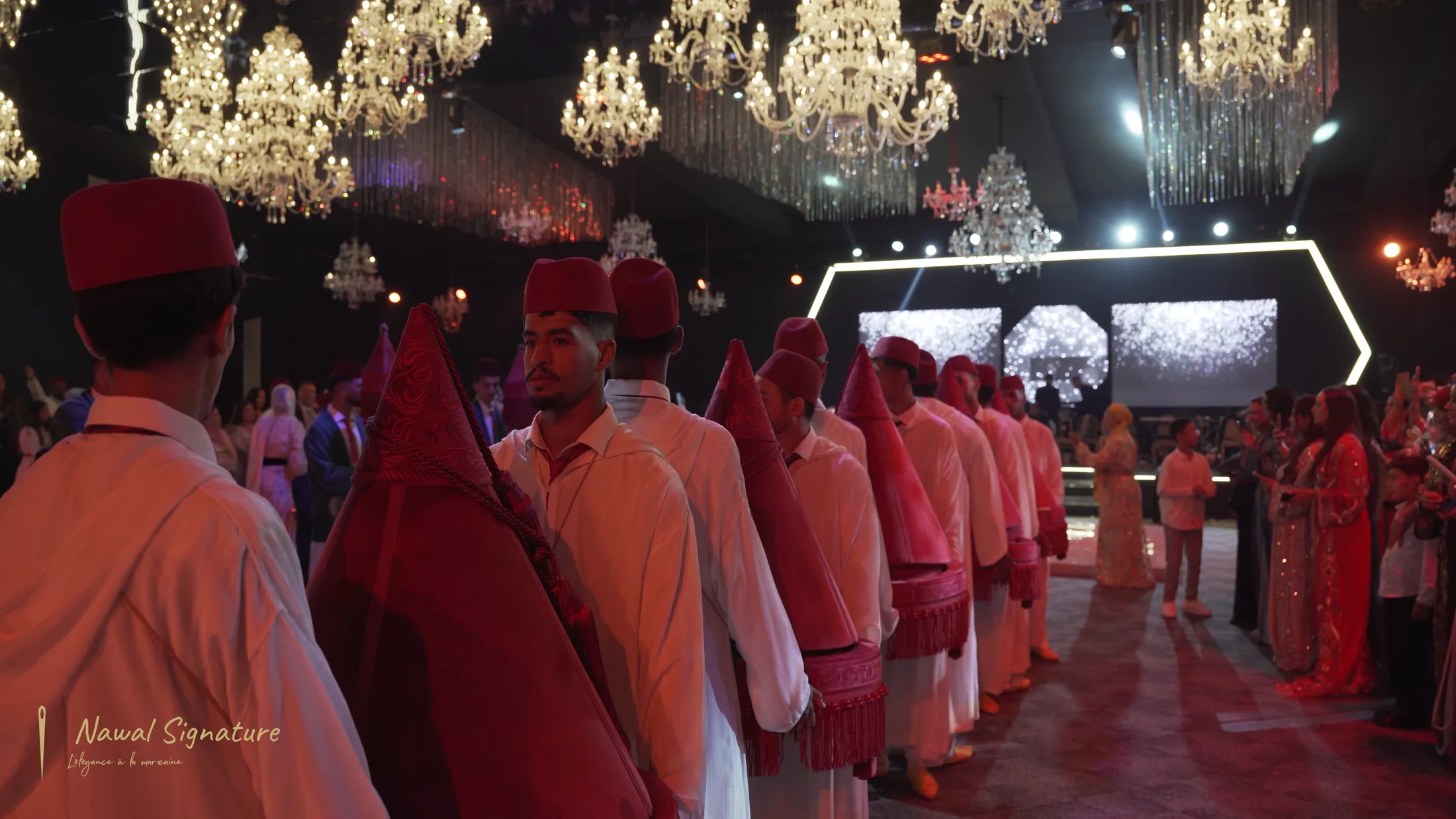 Défilé de porteurs en fez dans une salle illuminée de lustres